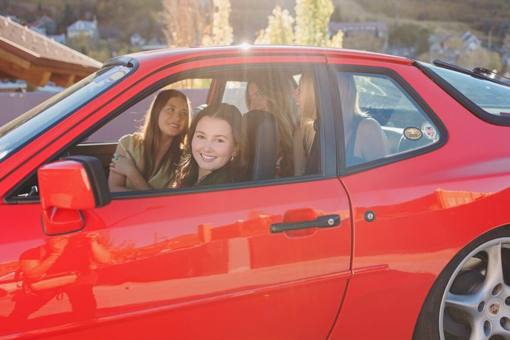 Group of stylish high school seniors posing with a vintage red Porsche in downtown Park City, Utah, for a senior rep team photoshoot.