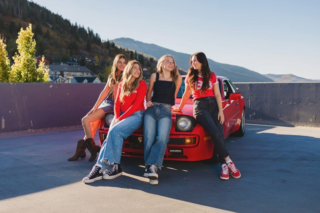 Group of stylish high school seniors posing with a vintage red Porsche in downtown Park City, Utah, for a senior rep team photoshoot.